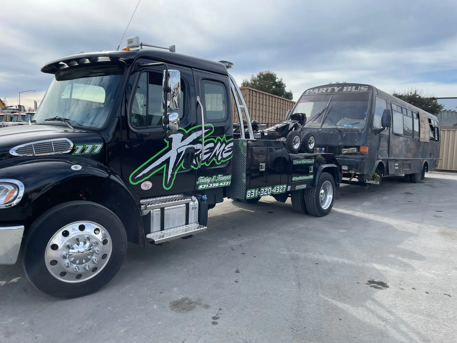 Black Xtreme Towing & Transport tow truck with green lettering, a dark bus hooked to its rear lift.